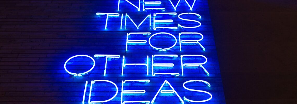 Blue text in neon on a brick wall reads "New times for other ideas." The photo is shot from below.